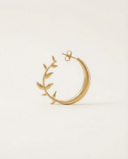 Gold moon earring with leaf design on a light beige background