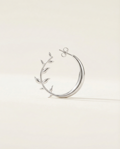 Silver moon earring with leaf-like designs on a light beige background