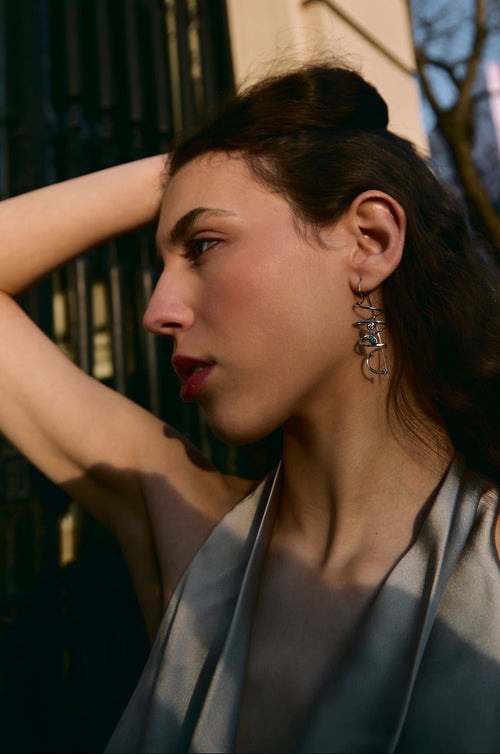 Woman with dark hair and earrings standing outdoors near a building