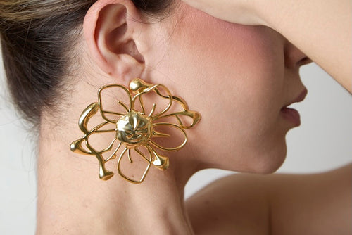 Woman wearing gold floral earrings and a matching ring on a neutral background