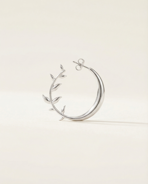 Silver moon earring with leaf-like designs on a light beige background